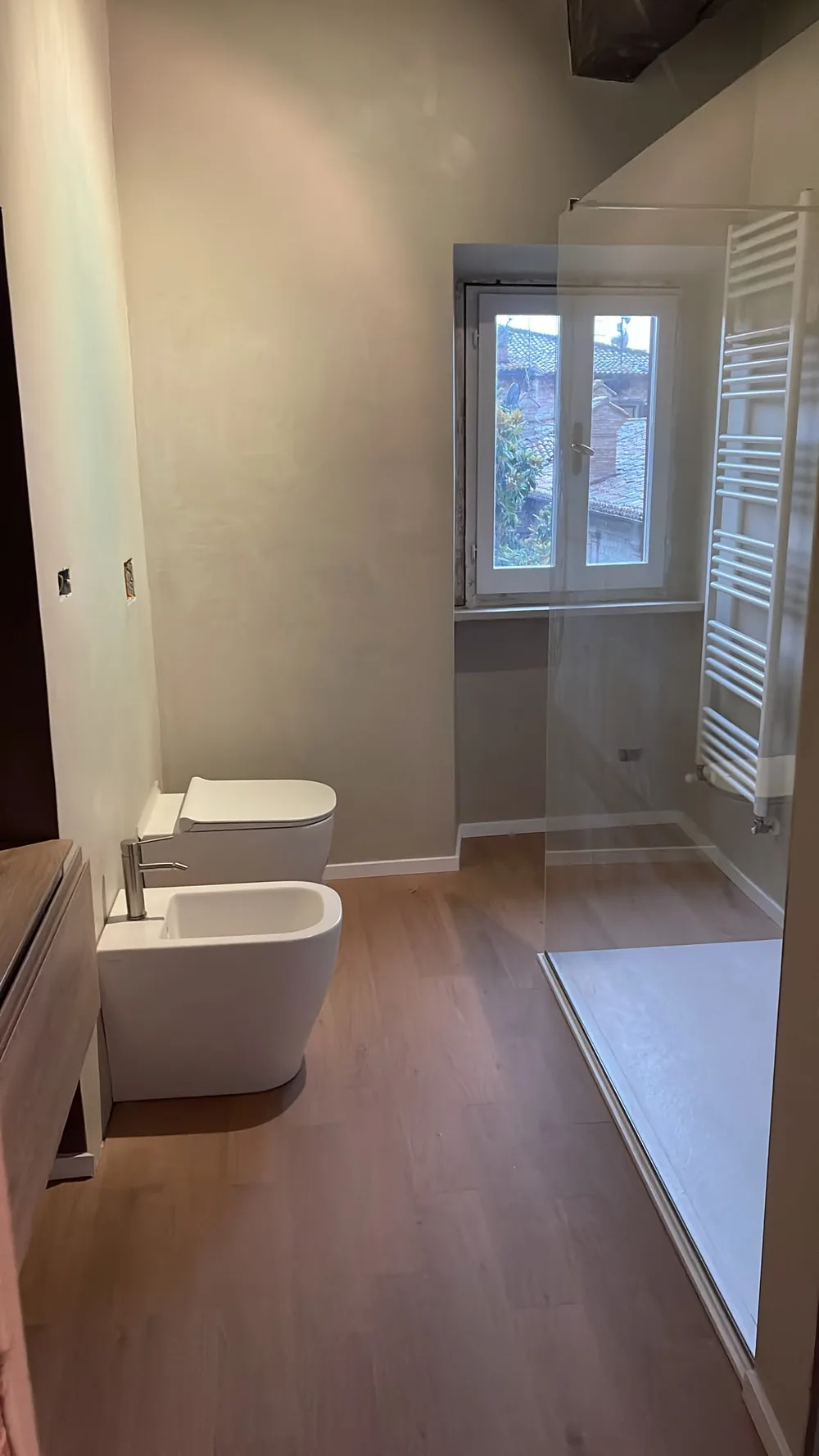 Bagno con doccia a vetro, termoarredo e finestra su tetti in cotto